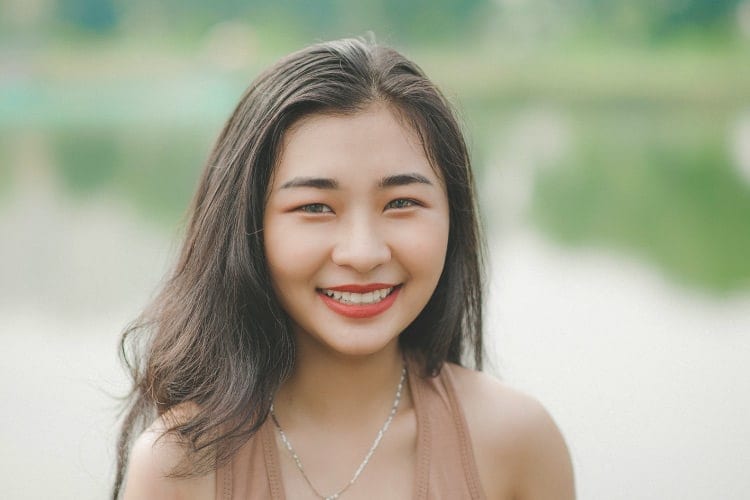 Close-up of smiling dark haired woman with red lipstick, white teeth, silver necklace, and pink tank top