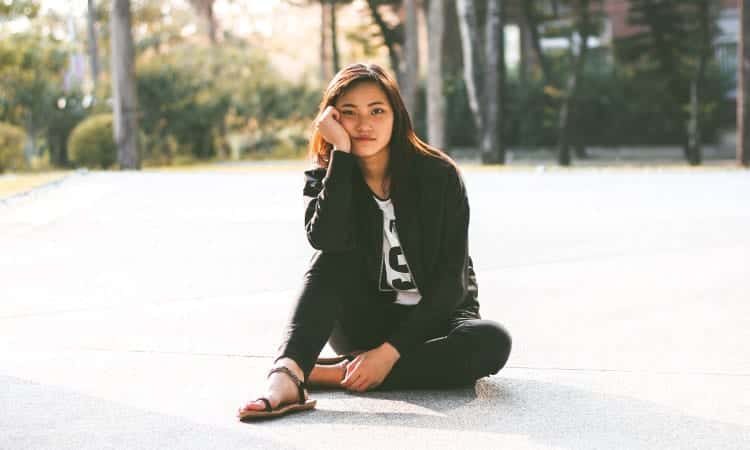 Brunette young woman wearing black and white sits on a large sidewalk with her hand on her cheek