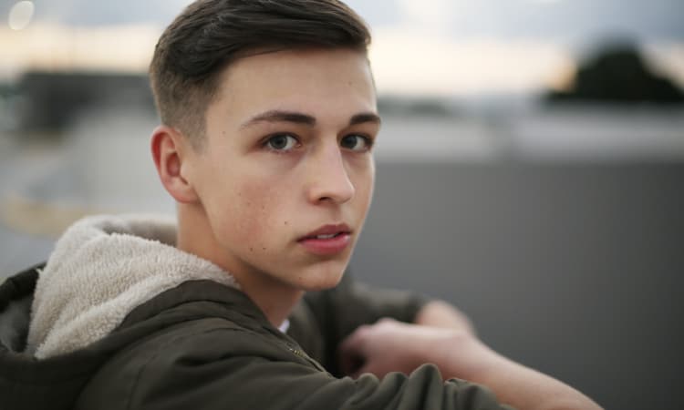 Teenage boy wearing an olive green jacket looks anxious as he worries about receding gums