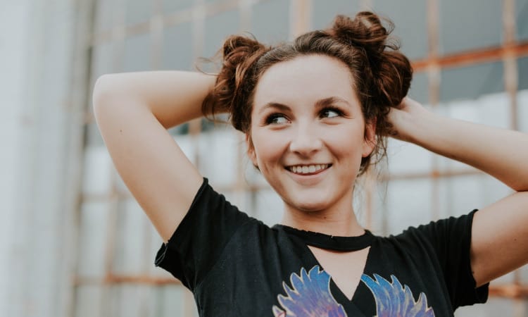 Brunette young woman wears her hair in two buns on the top of her head and smiles as she looks to the side