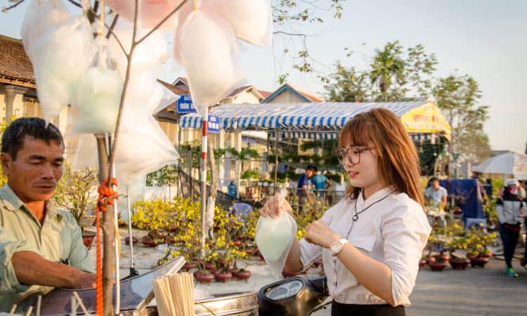 Brunette woman buys mint-colored cotton candy from a man at a cart at a market