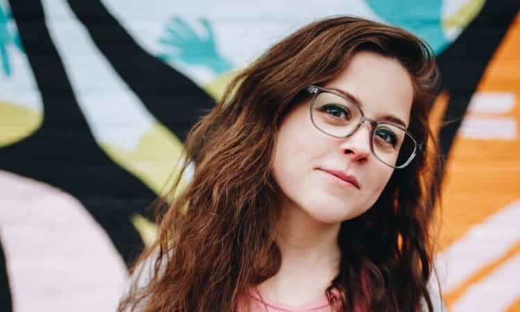 Brunette young woman wearing glasses leans her head to one side wondering when her wisdom teeth should be removed